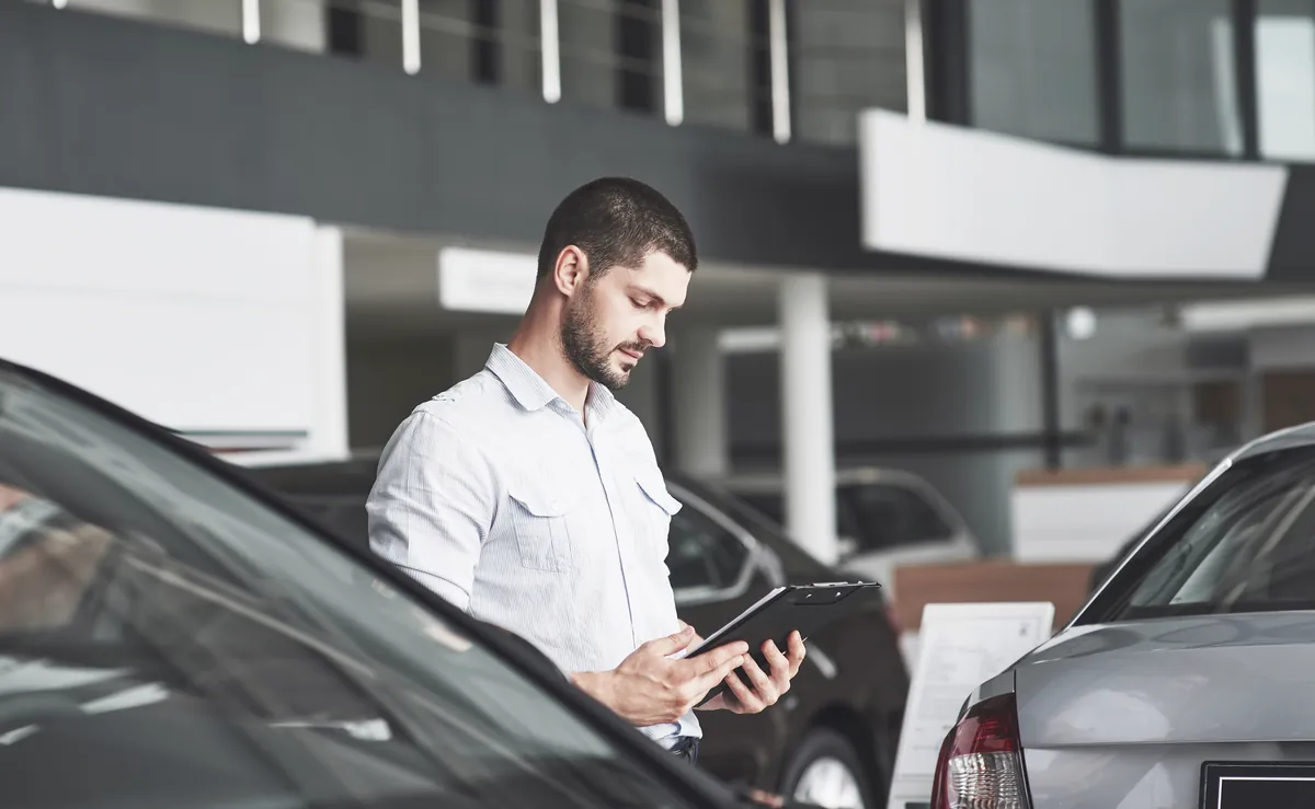 Mitarbeiter einer Autovermietung prüft Mietwagen mit dem Tablet bei Übergabe und Rücknahme