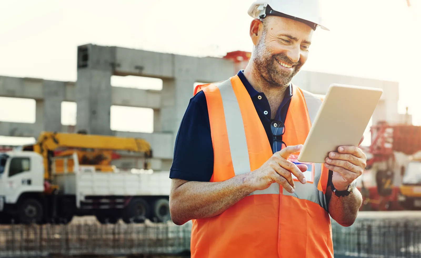 Bauleiter mit Helm plant auf dem Tablet auf der Baustelle – Aufträge gewinnen in der Baubranche