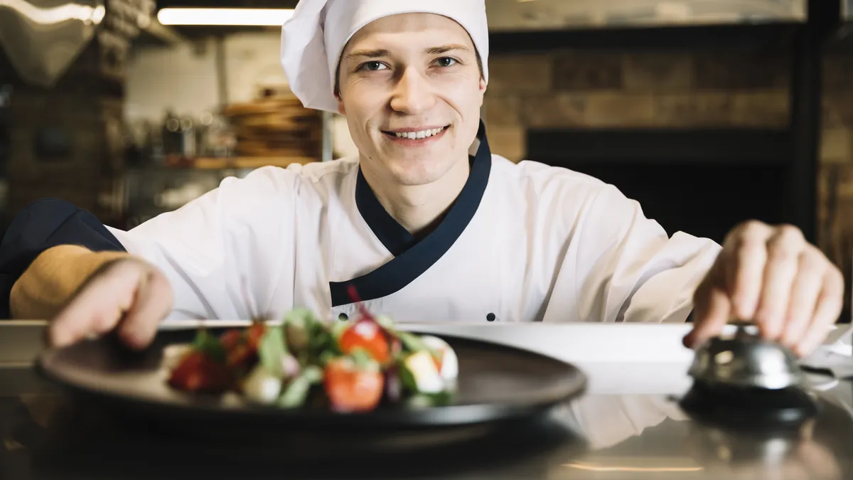 Koch richtet einen Teller am Pass an und läutet die Serviceglocke – Restaurantküche