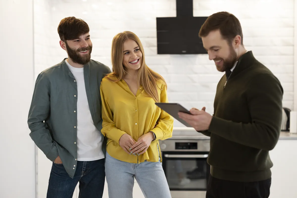 Makler zeigt einem Paar Details auf dem Tablet in der Küche – Immobilienberatung vor Ort