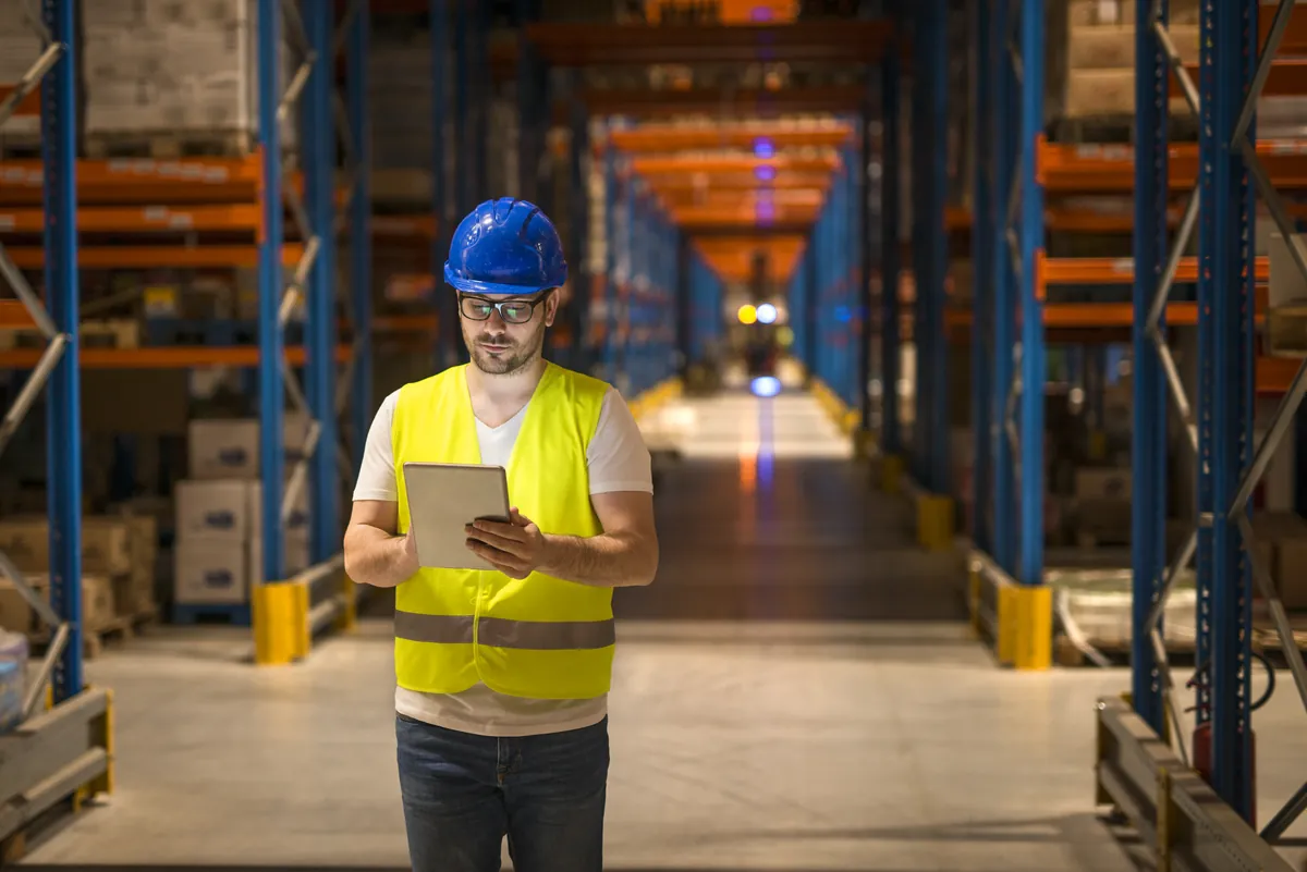 Lagerlogistiker kontrolliert Bestände mit dem Tablet im Hochregallager – Logistik digital steuern