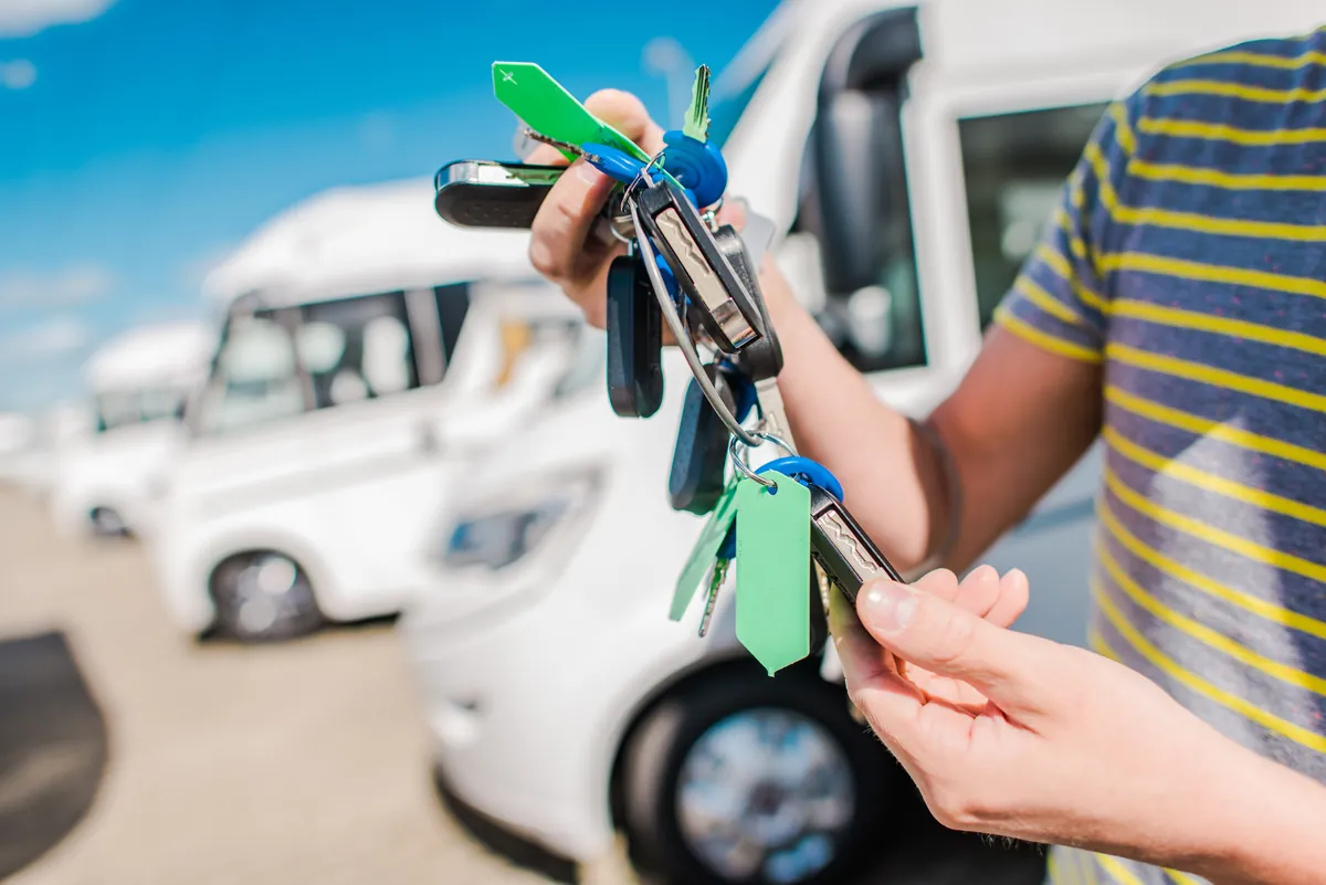 Mitarbeiter der Wohnmobilvermietung übergibt Schlüssel vor einer Reihe von Mietwohnmobilen